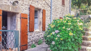 Un edificio in pietra con persiane di legno, un cancello in metallo e una fioriera con fiori gialli e viola.