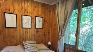 A wooden-paneled room with a large bed, three framed artworks on the wall, and a window with curtains. - Casa Tuwa Cabañas en pucón (Pucón)
