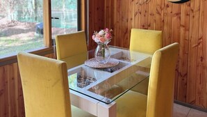 A dining area with a glass table and yellow chairs, a wooden wall, and a mirror with dried plants. - Casa Tuwa Cabañas en pucón (Pucón)