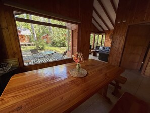 A wooden interior with a large window, a wooden table with a vase, and a view of an outdoor seating area. - Casa Tuwa Cabañas en pucón (Pucón)