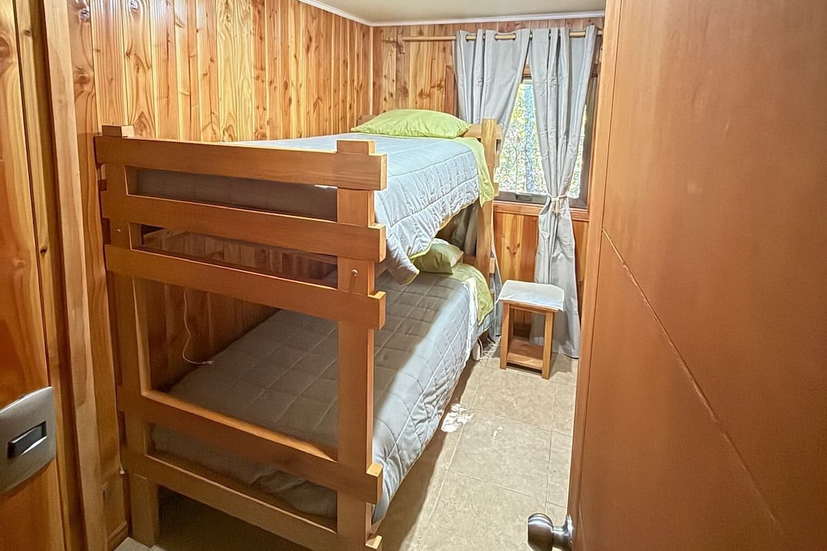 A room with a bunk bed, wooden panel walls, a small table, and a curtain.