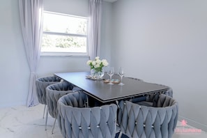 A dining area with a rectangular table, six upholstered chairs, a vase with white flowers, and two wine glasses.
