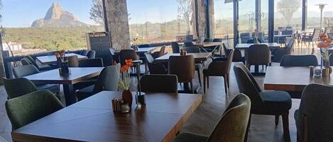 A restaurant with a view of a mountain. Tables and chairs are arranged indoors.