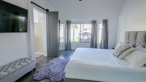 Ein modernes Schlafzimmer mit einem großen Bett, einer Sitzecke mit einer gepolsterten Couch, einem flachbildfernseher an der Wand und Blick ins Freie durch große Fenster.