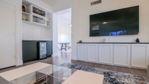 Ein modernes Wohnzimmer mit einem Glastisch, weißen Schränken und einem großen Flachbildfernseher an der Wand.