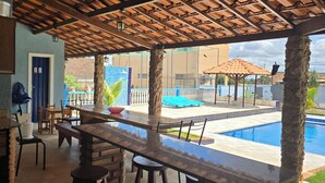 A covered outdoor dining area with a pool, wooden furniture, and a view of the pool. - BomjaMinas property, swimming pool, bed linens and towels, 17 km from Inhotim. (Mário Campos)