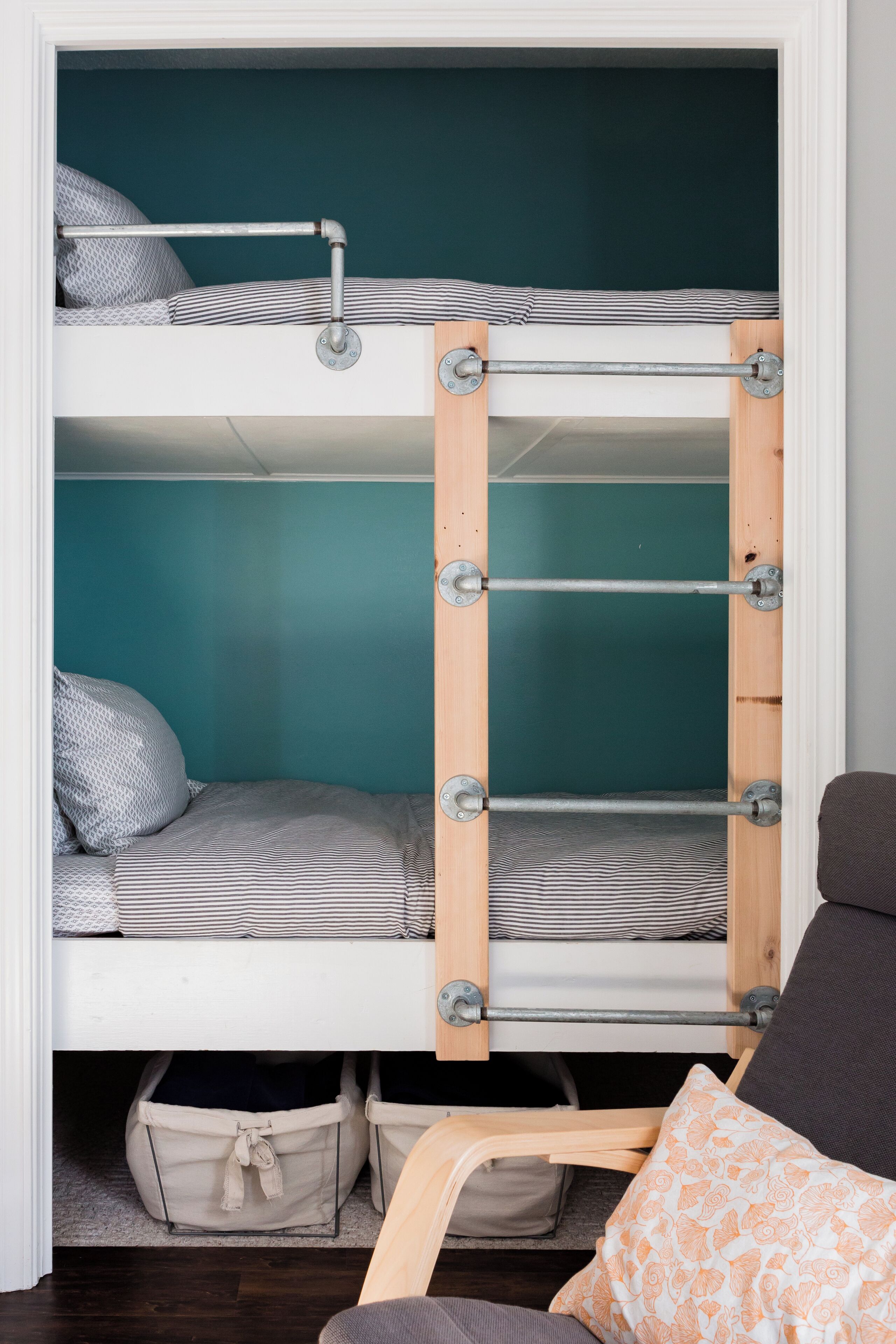 Ein Stockbett mit einer Metallleiter, einer türkis gefärbten Wand und einem Holzstuhl mit Kissen.