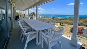 A covered outdoor dining area with a table and chairs, overlooking a coastal landscape. - Spacious 6-bedroom villa with AC and large private pool (Christiansted)
