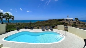 A swimming pool with lounge chairs, surrounded by a concrete deck, overlooking a coastal landscape. - Spacious 6-bedroom villa with AC and large private pool (Christiansted)