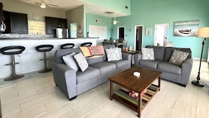 A spacious living room with two grey sofas, a wooden coffee table, and a kitchen area with a bar counter and stools. - Spacious 6-bedroom villa with AC and large private pool (Christiansted)