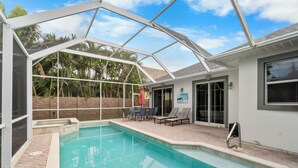 A covered swimming pool with a patio area, a table, chairs, and a red umbrella. - 🏖️ 4BR Beach House w/ Heated Spa and Pool (Naples)