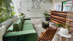En moderne lobby med en grøn sofa, træstole, en receptionsdisk og et geometrisk vægkunstværk.