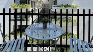En balkon med et rundt bord og to stole, omgivet af et sort metalhegn.