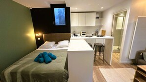 A compact hotel room with a bed, a small kitchenette, a TV mounted on the wall, and a bathroom visible through an open door. - Studio Tourny, 2 pers, centre Bordeaux (BORDEAUX)