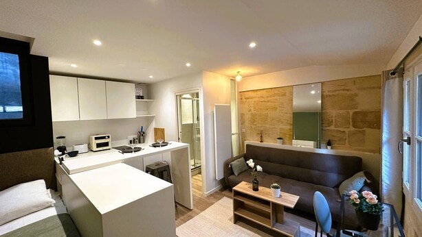 A modern kitchen with a central island, a dining area with a sofa, and a large mirror. - Studio Tourny, 2 pers, centre Bordeaux (BORDEAUX)