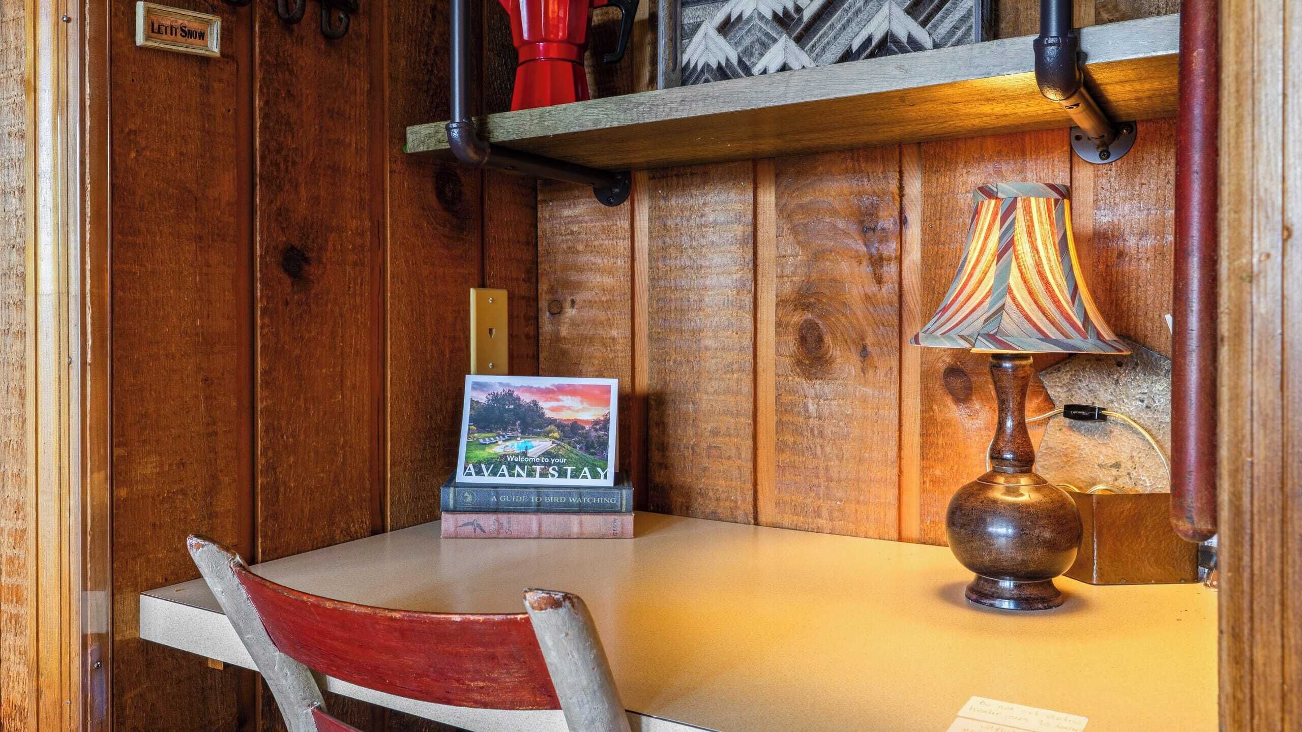 A wooden interior with a table, a lamp, a bird watching guidebook, and a red chair.
