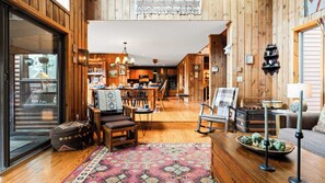 A cozy, wooden interior with a dining area, a living room with a sofa and a coffee table, and a kitchen in the background. - Secluded Retreat w/ Pool, Hot Tub, Fire Pit, Views Windham Mountain House (Windham)