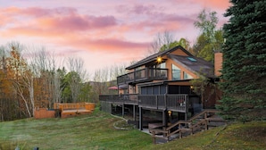 A two-story wooden house with a deck and a covered outdoor area, surrounded by trees and a grassy yard. - Secluded Retreat w/ Pool, Hot Tub, Fire Pit, Views Windham Mountain House (Windham)
