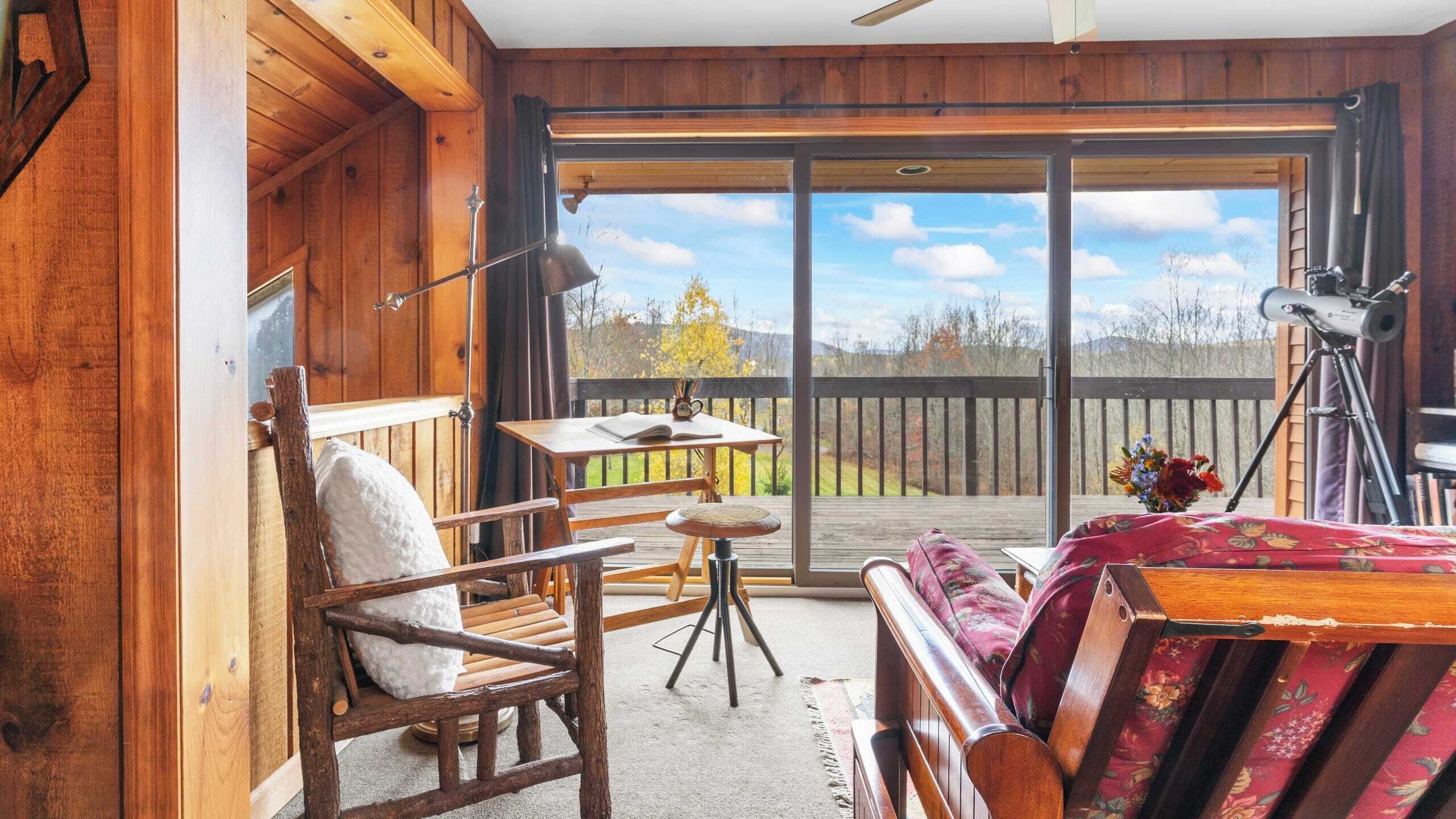 A cozy cabin interior with a wooden deck, a dining table, a chair, a sofa, and a telescope.