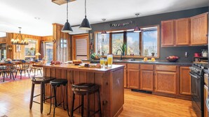 Una cucina moderna con mobili in legno, un'isola centrale con sgabelli, un'ampia finestra e vista sugli alberi.