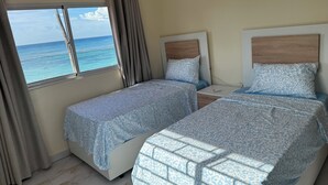 Un dormitorio con dos camas, una ventana con cortinas y vista al océano.