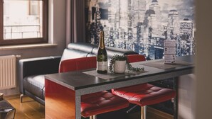 Una sala de estar moderna con un sofá rojo, una mesa de comedor con una botella de vino y un mural de paisaje urbano en la pared.