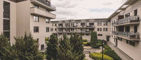 A multi-story residential building with balconies, a courtyard with trees, and a clear sky.