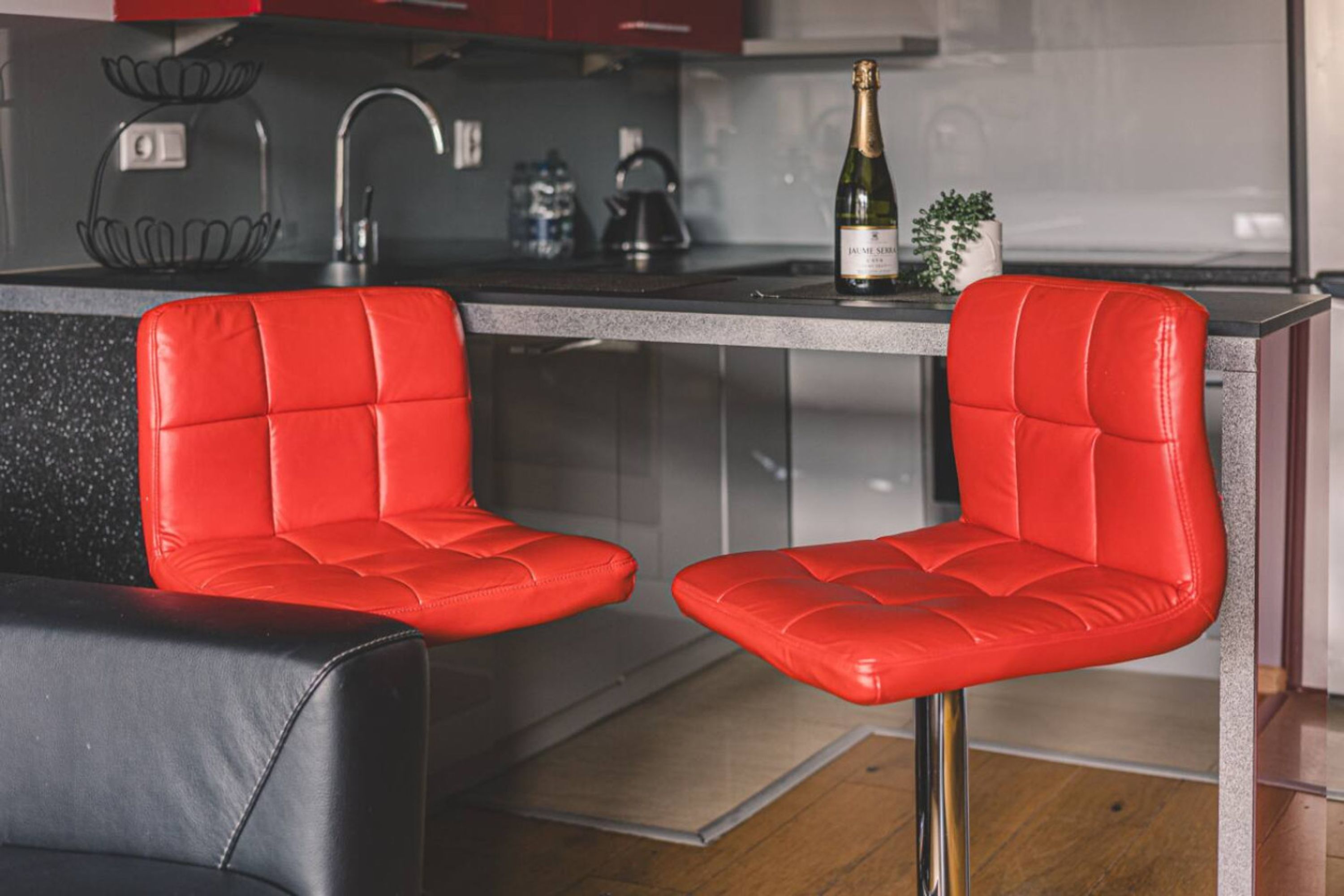 A modern kitchen with two red leather bar stools, a stainless steel sink, and a bottle of champagne on the counter.