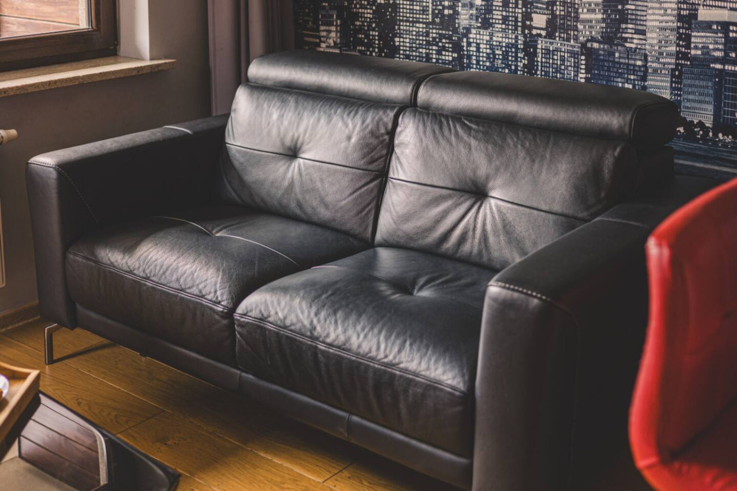 A black leather sofa in a room with a cityscape view through a window.