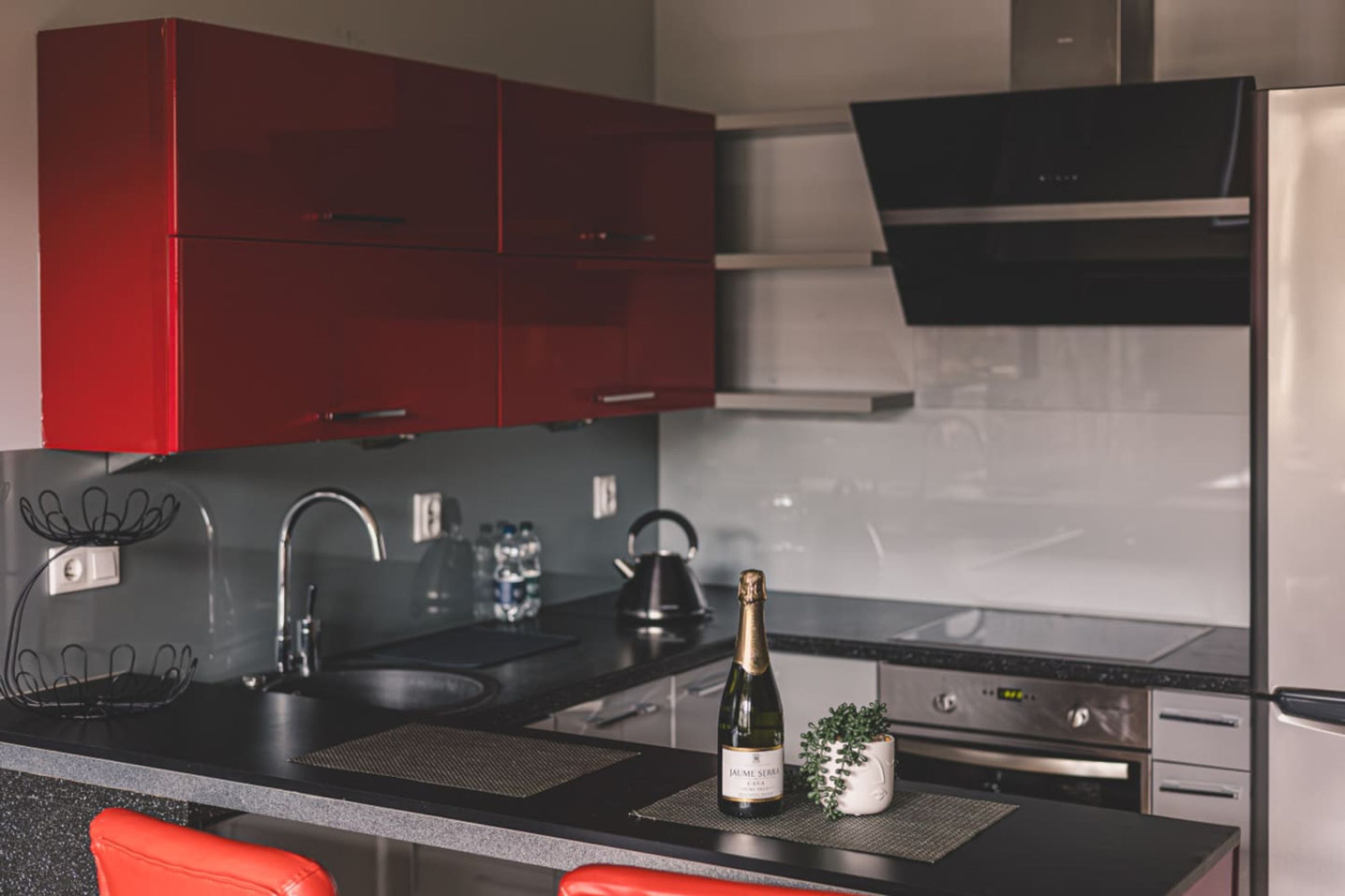 A modern kitchen with red cabinets, a stainless steel refrigerator, and a bottle of champagne on the counter.