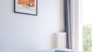 Une chambre d’hôtel avec un lit, un radiateur, une fenêtre avec des rideaux et une affiche encadrée au mur.