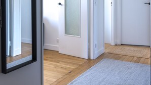Un couloir doté d’un plancher en bois, de murs blancs et d’un grand miroir. Des portes donnent accès à d’autres pièces.
