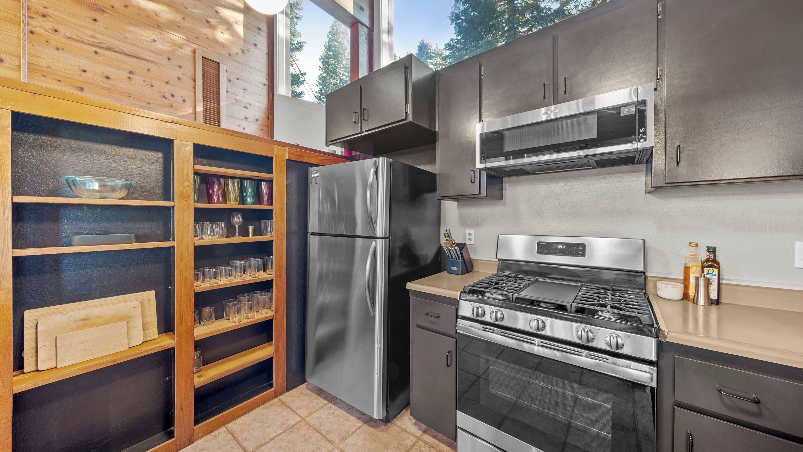 Una cocina moderna con electrodomésticos de acero inoxidable, estantes de madera y un amplio ventanal.