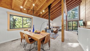 Una habitación amplia con techo de madera, ventanas grandes, un comedor con mesa y sillas, y una chimenea.