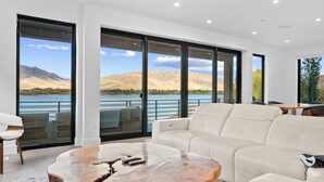 Ein modernes Wohnzimmer mit einem großen Fenster, das einen Blick auf einen See und Berge bietet.