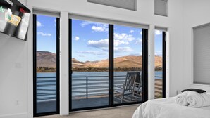 Ein Hotelzimmer mit einer großen Schiebetür, die auf einen Balkon mit Blick auf einen See und Berge führt.
