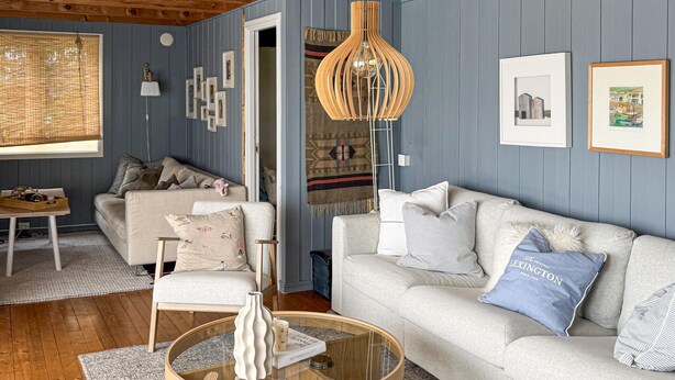 Een gezellige woonkamer met een bank, fauteuil en salontafel. Er hangen ingelijste foto's aan de muur en een hanglamp.