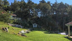 Een gazon met een kleine witte prieel, een houten bank en een tuinhuis.