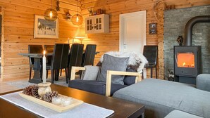 Een gezellig blokhutinterieur met een open haard, houten wanden en een eethoek met stoelen en een tafel.