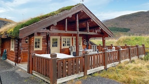 Een rustieke blokhut met een veranda, stenen fundering en een rieten dak.