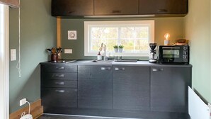 A modern kitchen with dark cabinetry, a window with a view of trees, a coffee maker, and a microwave. - 2 bedroom cozy home in Straumgjerde (Straumgjerde)