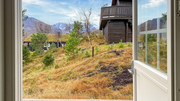 A view from inside a building looking out to a mountainous landscape with a wooden structure and a small building with a thatched roof. - 2 bedroom cozy home in Straumgjerde (Straumgjerde)