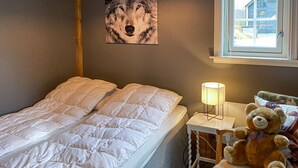 A bedroom with a bed, a nightstand with a lamp, a teddy bear, and a window with a view of a house. - 2 bedroom cozy home in Straumgjerde (Straumgjerde)
