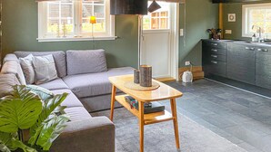 A modern living room with a grey sofa, a wooden coffee table, and a kitchen area with dark cabinets and a window. - 2 bedroom cozy home in Straumgjerde (Straumgjerde)