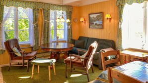 A cozy room with a round wooden table, two chairs, a sofa, and a window with curtains.