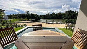 Une table et des chaises en bois sur une terrasse offrant une vue sur un lac et une plage.