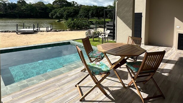 Une terrasse extérieure avec une piscine, des meubles en bois et une vue sur une plage et des arbres.