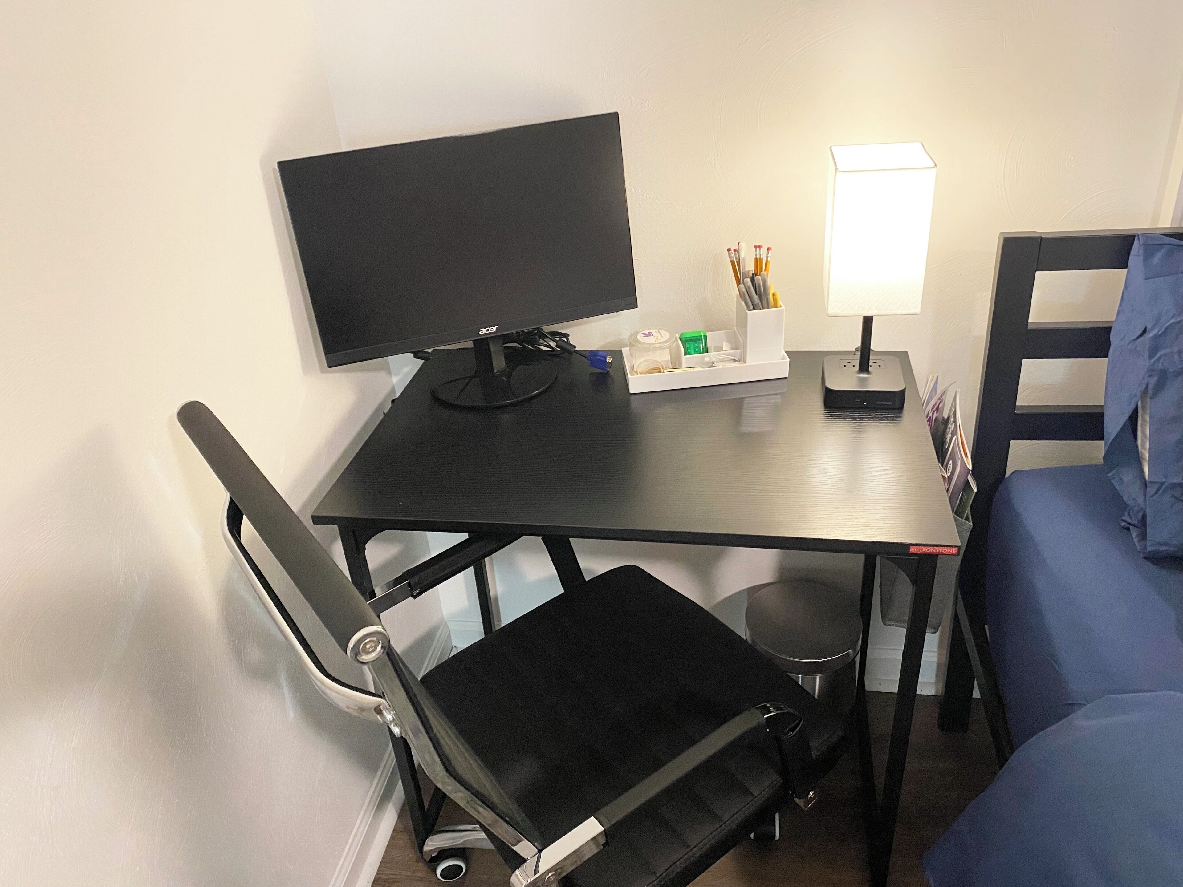 Een kleine, compacte kamer met een bureau, een stoel, een bed en een bureaulamp.
