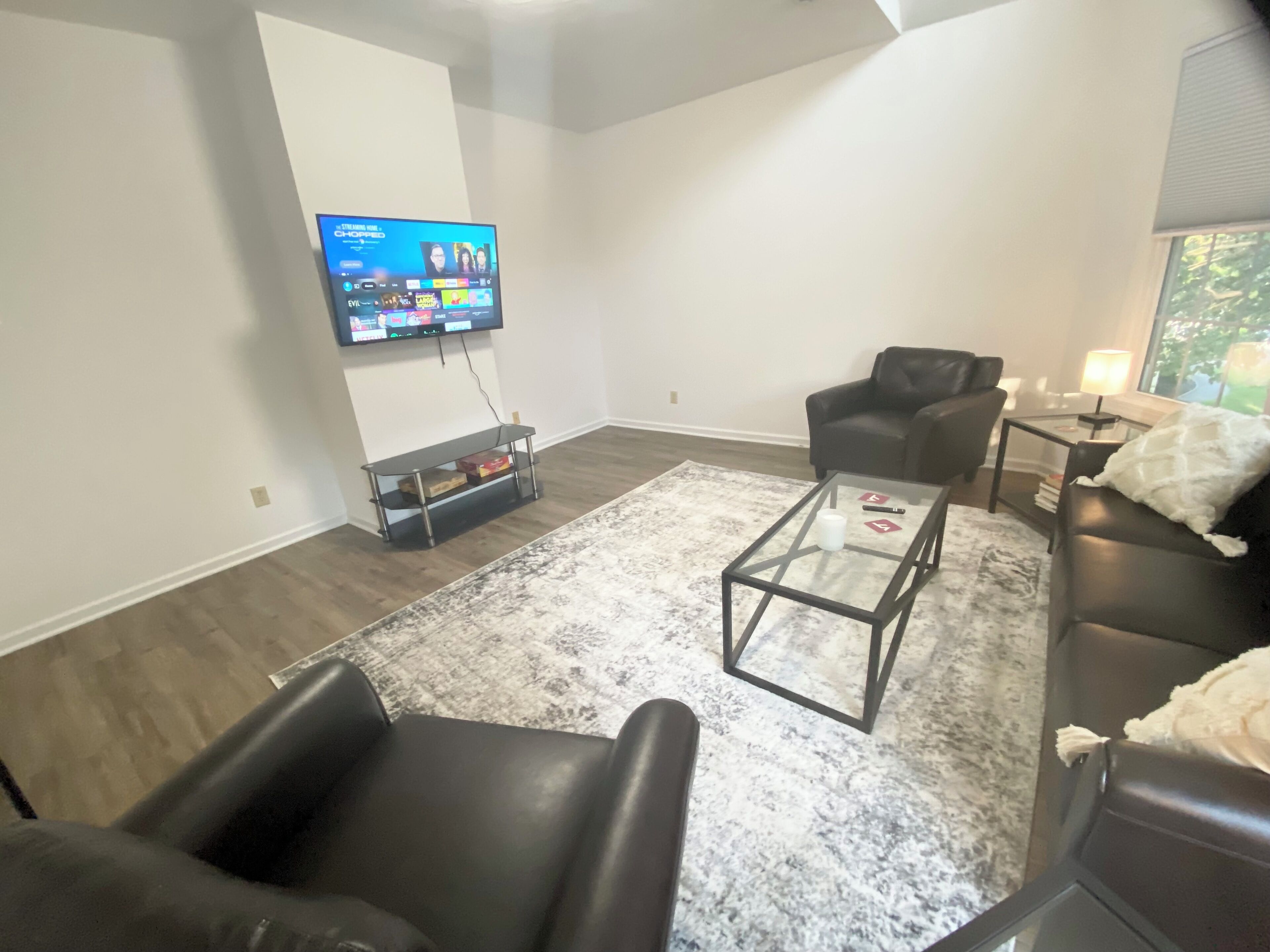 Un salon moderne avec un téléviseur à écran plat fixé au mur, une table basse en verre, un canapé en cuir et un fauteuil noir.