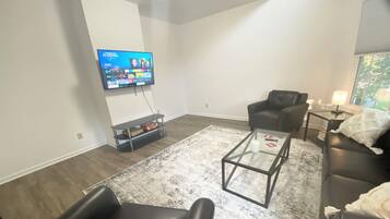 Un salon moderne avec un téléviseur à écran plat fixé au mur, une table basse en verre, un canapé en cuir et un fauteuil noir.
